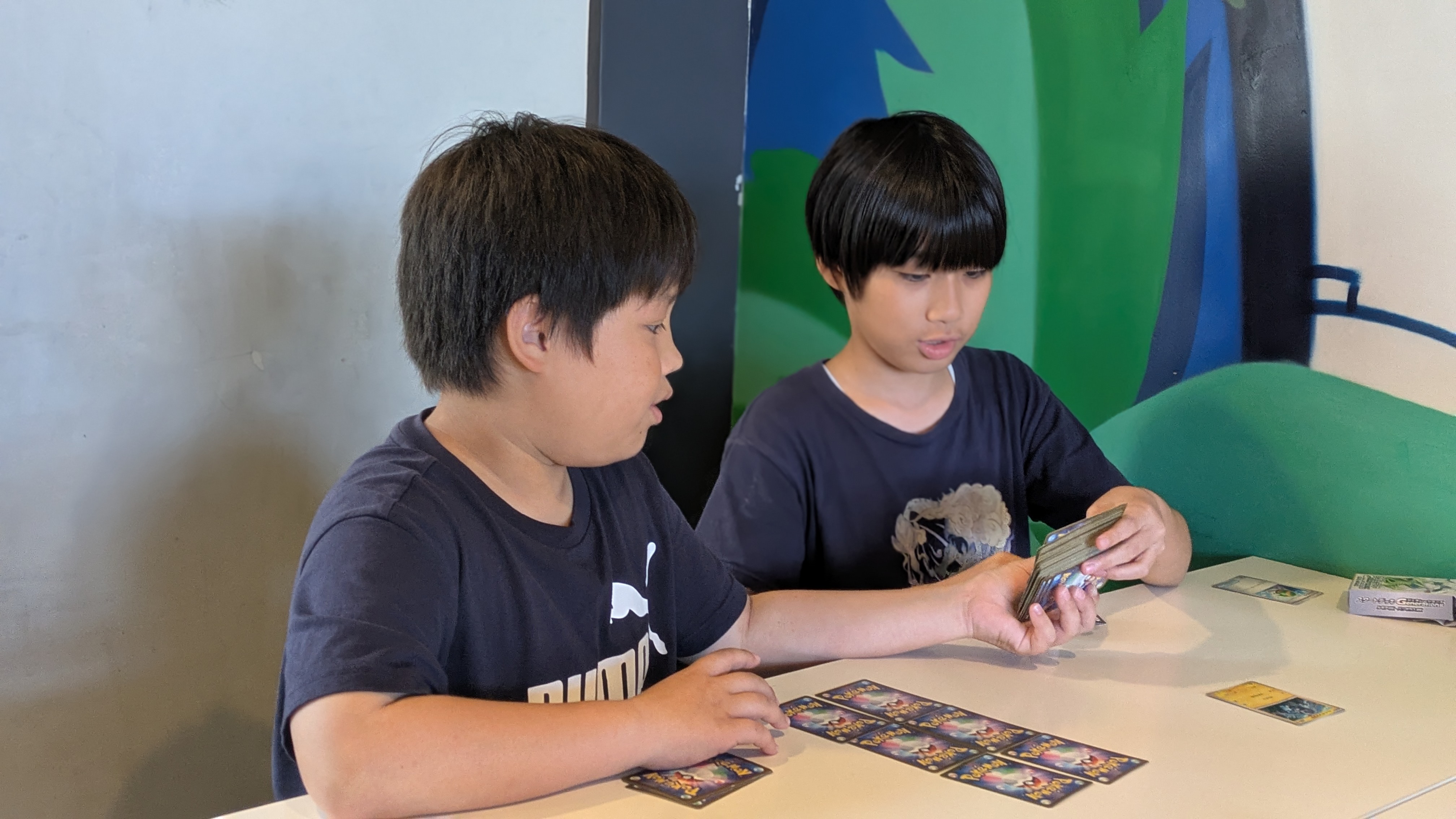 放課後等デイサービス SOU NEXT ジュニア志真志(宜野湾市志真志)の清潔なプレイルーム内にて、複数人の子どもたちがテーブルを囲み、真剣な表情で木製のボードゲームをプレイしながら、お互いに『次はそっちの番だよ』と優しくルールを確認し合っている様子
