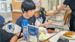 琉球大学の学食にて、周りに気をつけながらトレイを持って美味しく食事をする児童の様子