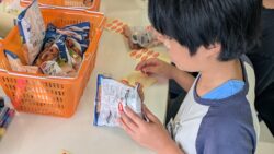 琉球大学生協の店頭で、真剣な表情で商品の品出しやレジ打ちの職場体験をする子どもの手元